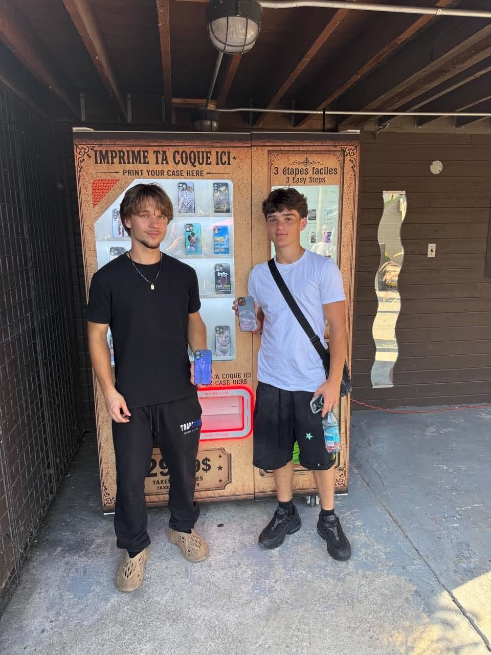 Deux amis tenant leurs coques personnalisées devant la borne